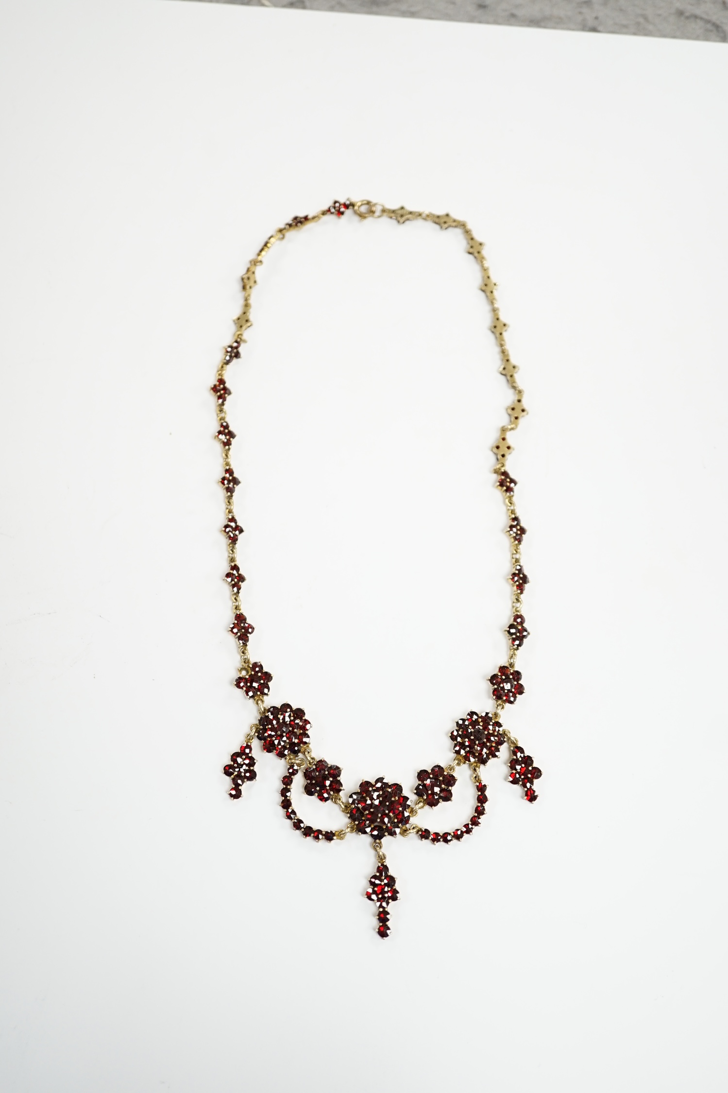 An early 20th century gilt sterling and garnet cluster set drop necklace, 45cm.